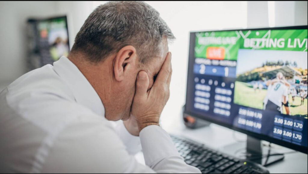 Frustrated man reacting to sports betting loss on computer screen